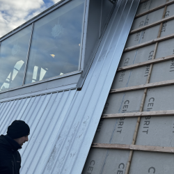 Arbejder monterer nyt tagpanel på bygningens facade.